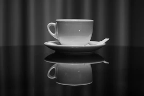 A sleek black tea cup with a smooth matte finish paired with a matching saucer on a dark wooden table