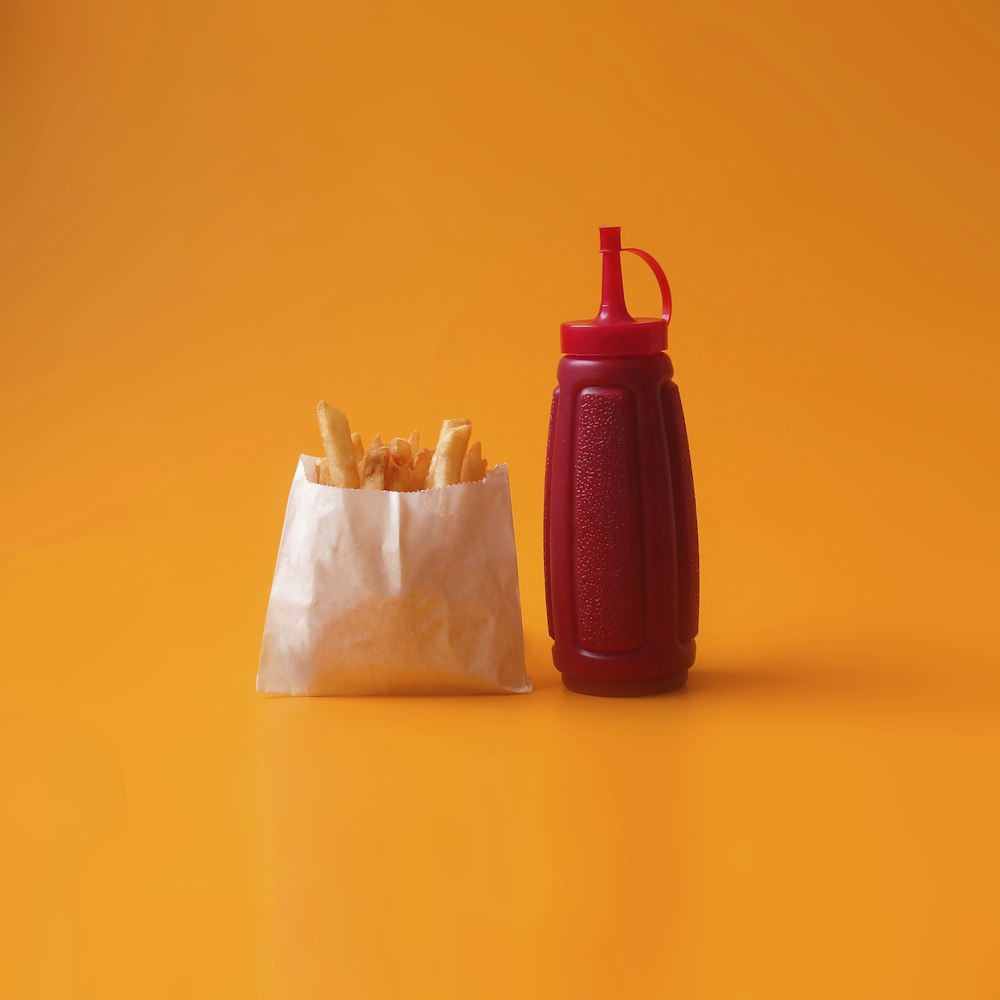 Frittierte Pommes in weißer Packung neben roter Quetschflasche