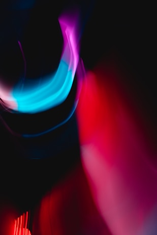 Abstract image featuring vibrant, flowing streaks of light in shades of blue, pink, and red against a dark background. The composition creates a sense of motion and energy.