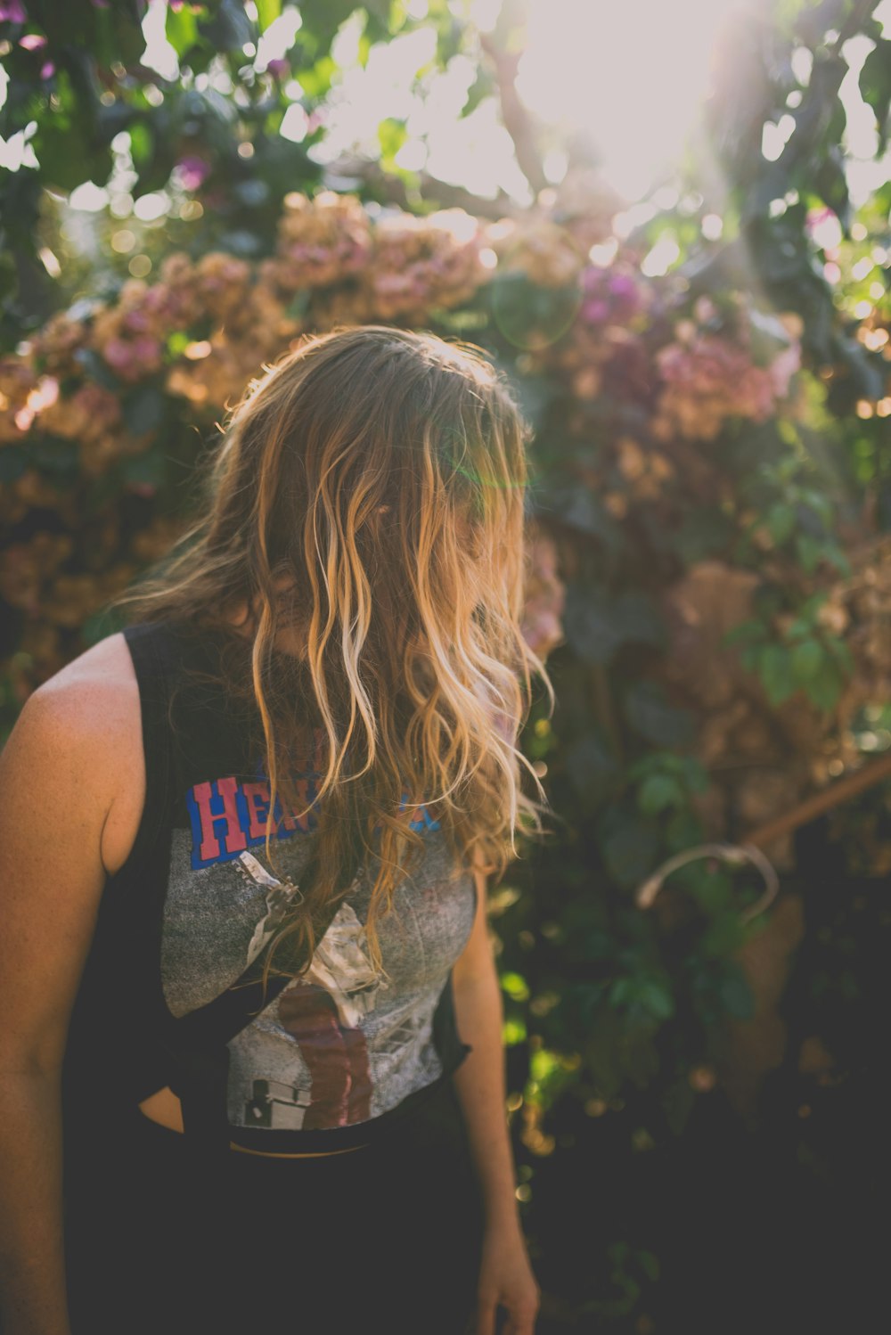 person wearing black sleeveless top near pink flower plant