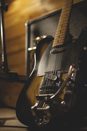 A close-up view of an electric guitar resting against an amplifier, with warm lighting highlighting the wood grain and metallic components.