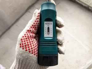 Hands wearing gloves holding a heavy-duty wrench in a factory setting.