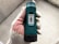 A hand wearing a white glove with red dotted patterns is holding a green torque wrench. The wrench has a black grip and a white dial displaying numerical settings ranging from 1 to 8 marked as 'MOMENT'. The background is a blurred concrete surface.