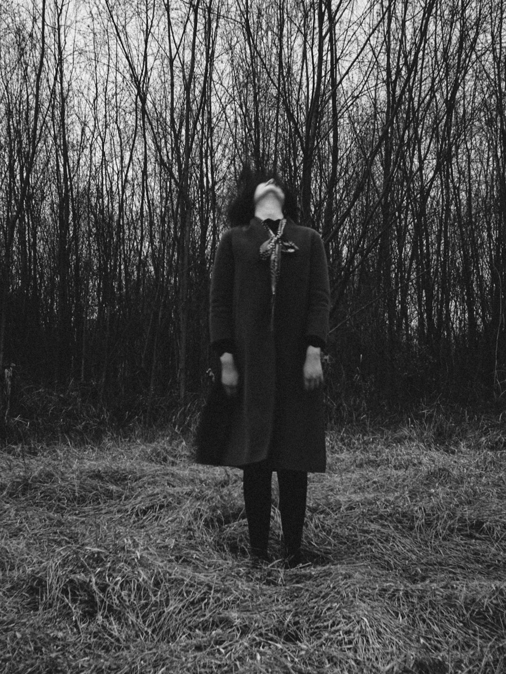 grayscale photo of man standing in the middle of the forest