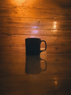 A sleek black mug held in hand against a backdrop of morning sunlight streaming through a window