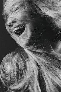 A dynamic black and white photograph captures a close-up of a person's face partially obscured by flowing hair. The person is smiling broadly, conveying a sense of joy and movement.