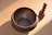 A metal singing bowl with intricate designs rests on a surface, accompanied by a wooden mallet with a rounded handle. The setup is illuminated by natural light, creating soft shadows.