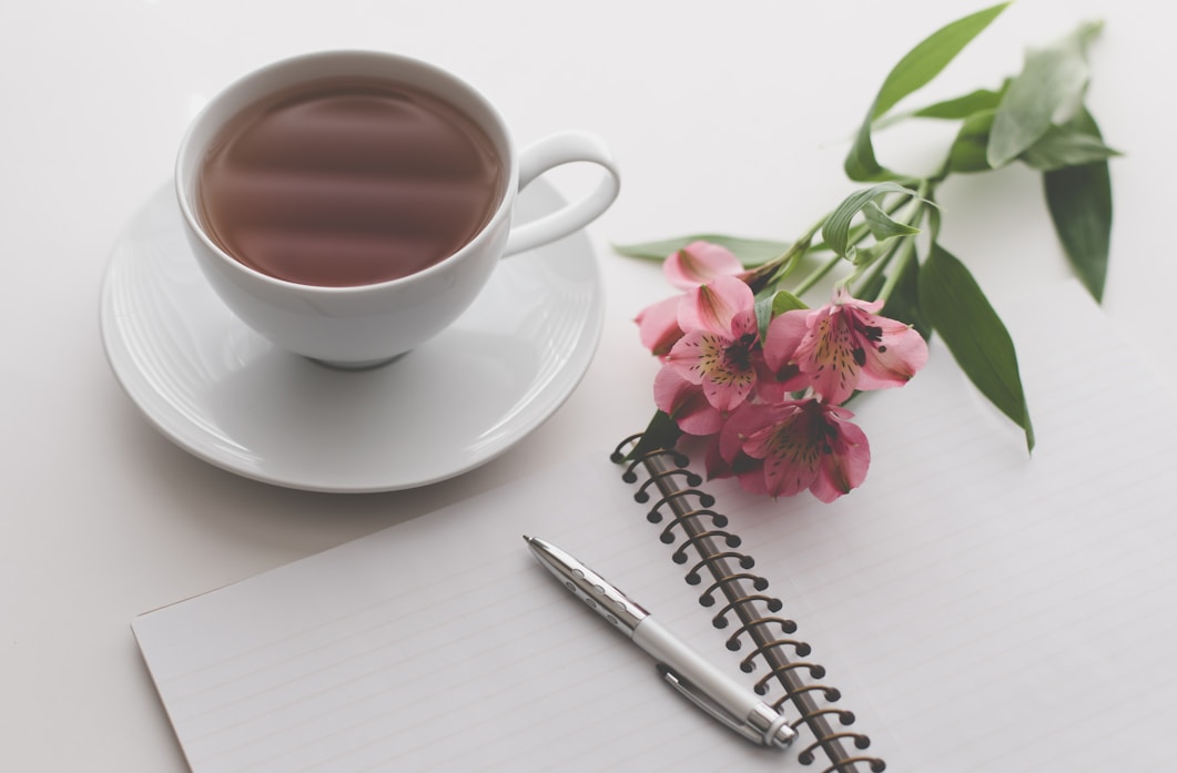 white teacup filled with brown liquid near pink flower