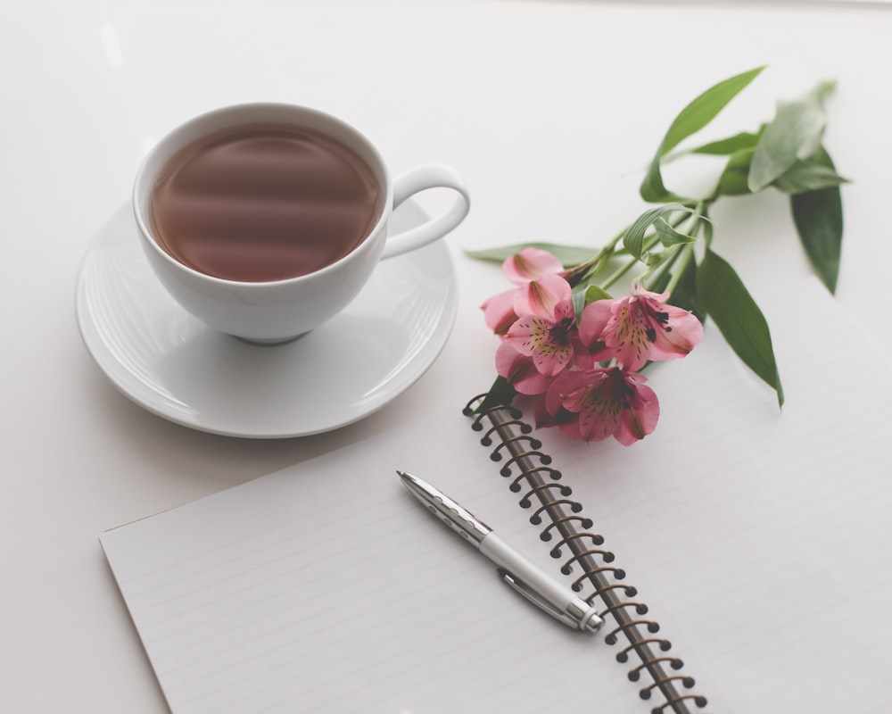 tasse de thé blanche remplie d’un liquide brun près de la fleur rose