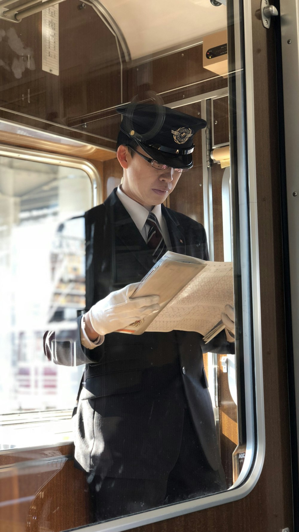 man in black uniform reads paper white standing inside train