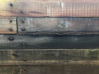 Weathered horizontal wooden planks fastened with square-head bolts, showcasing a rustic and worn texture.