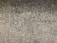 A close-up view of an aggregate concrete surface composed of a mix of small pebbles embedded in cement, creating a textured and rough appearance.