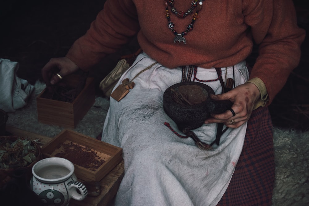 person in red sweater sits beside table with white tea cup