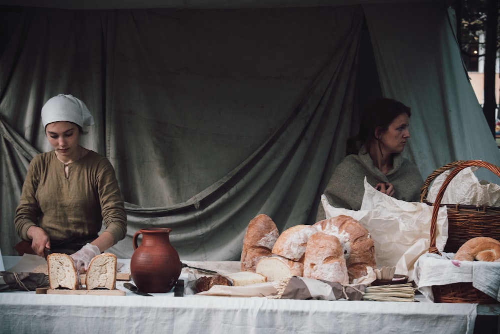 woman slicing bread beside woman standing beside basket