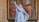 A marble statue of a religious figure is prominently displayed in front of a large painting. The statue portrays a person in flowing robes with one arm raised. The painting behind depicts a biblical scene with multiple figures dressed in historical attire, standing in a grand architectural setting.
