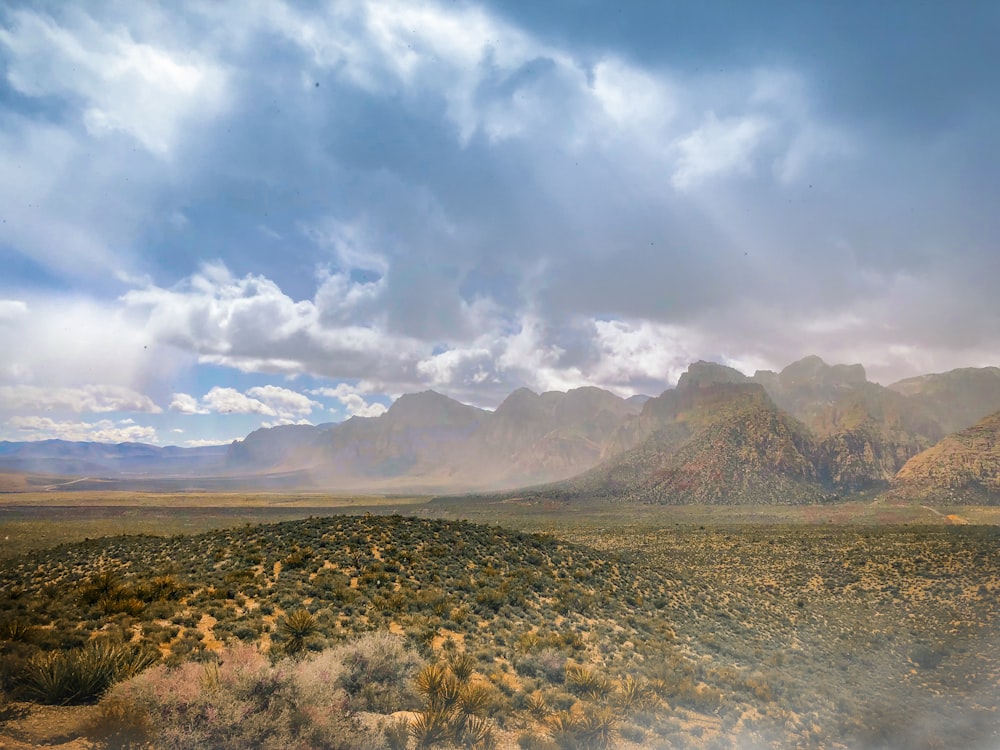 brown and green grass field near brown mountain under white clouds and blue sky during daytime