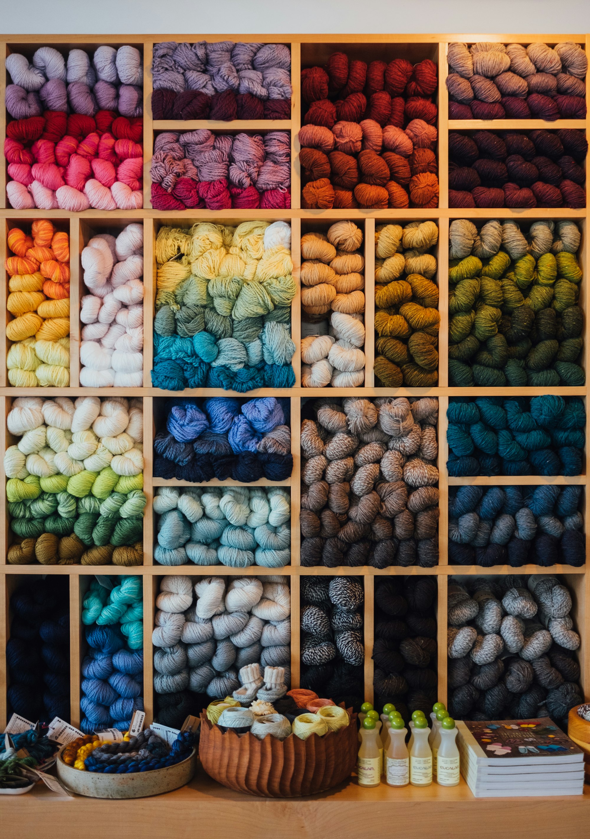 A bunch of different colors of yarn, sorted by color, sit bundled in cubbies.
