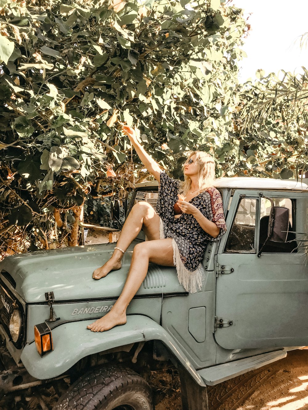 woman sitting on hood of parked grey classic Toyota Land Cruiser SUV