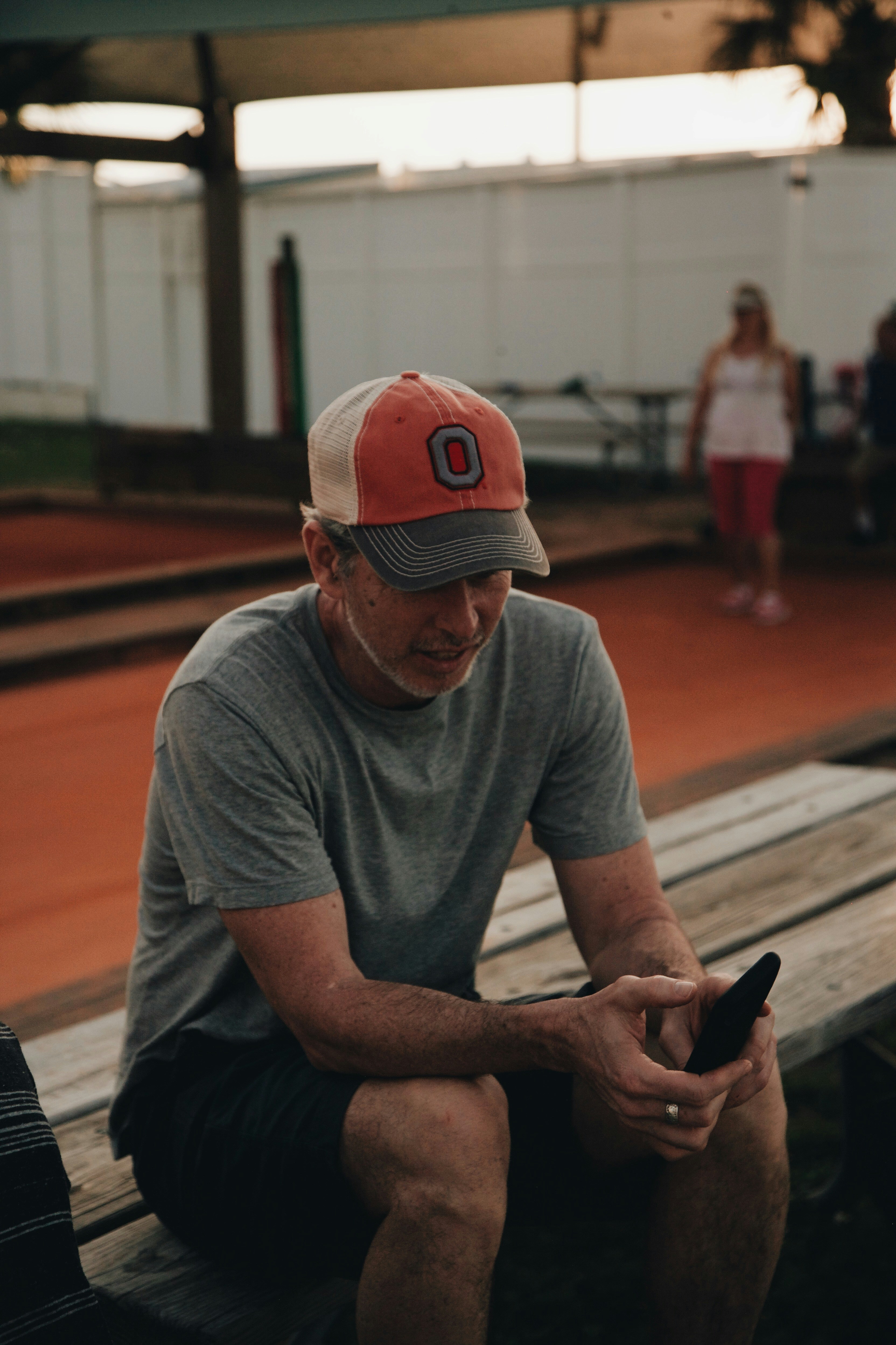 man wearing crew-neck t-shirt using smartphone while sitting on brown wooden bench