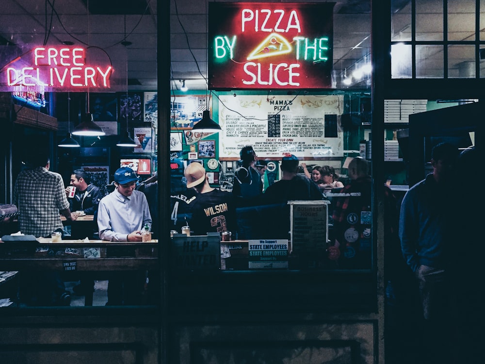 pizza by the slice neon sign hanged on glass panel