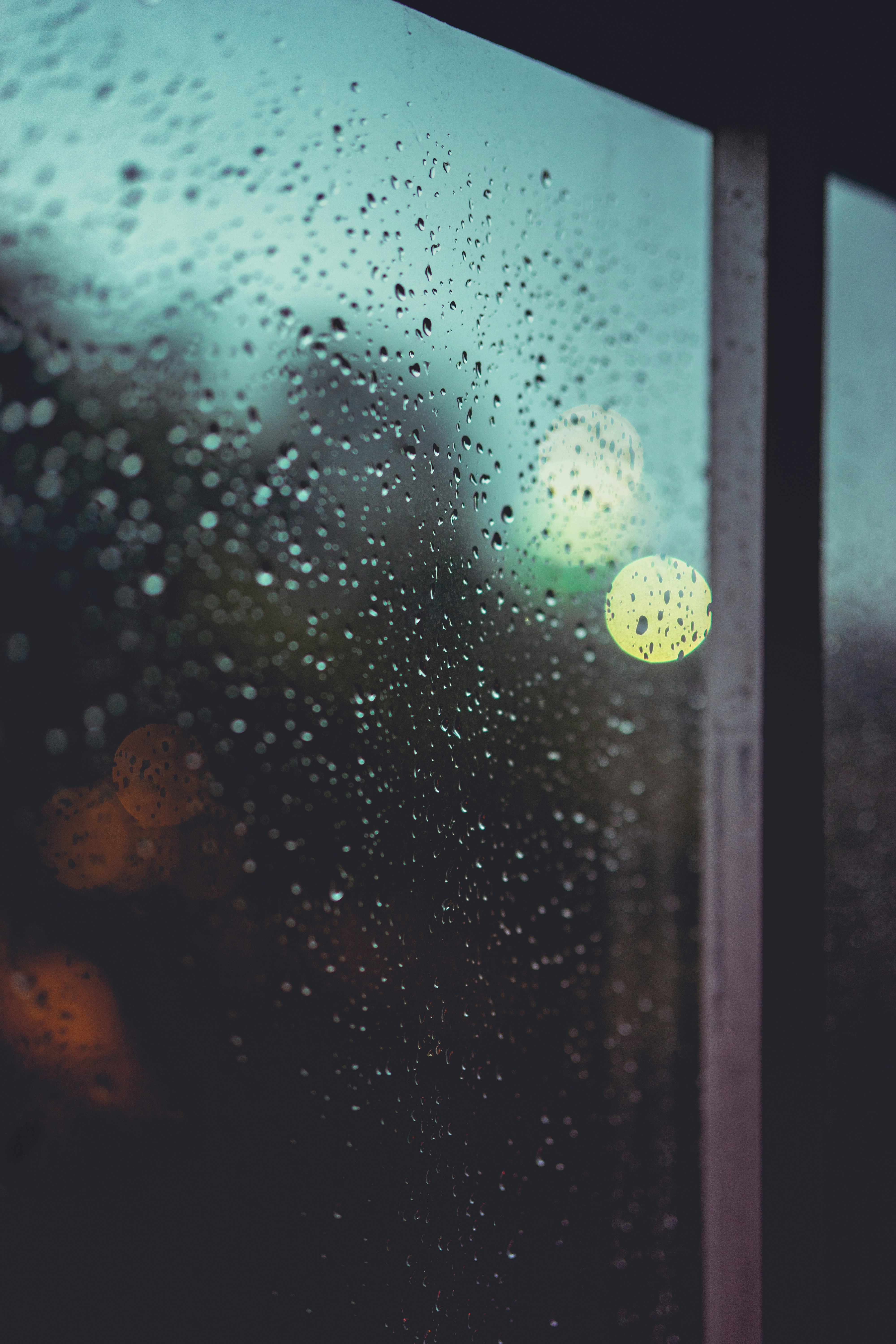 Rain drops on dark window glass at night, blurred city lights beyond, melancholy and contemplative atmospheric mood