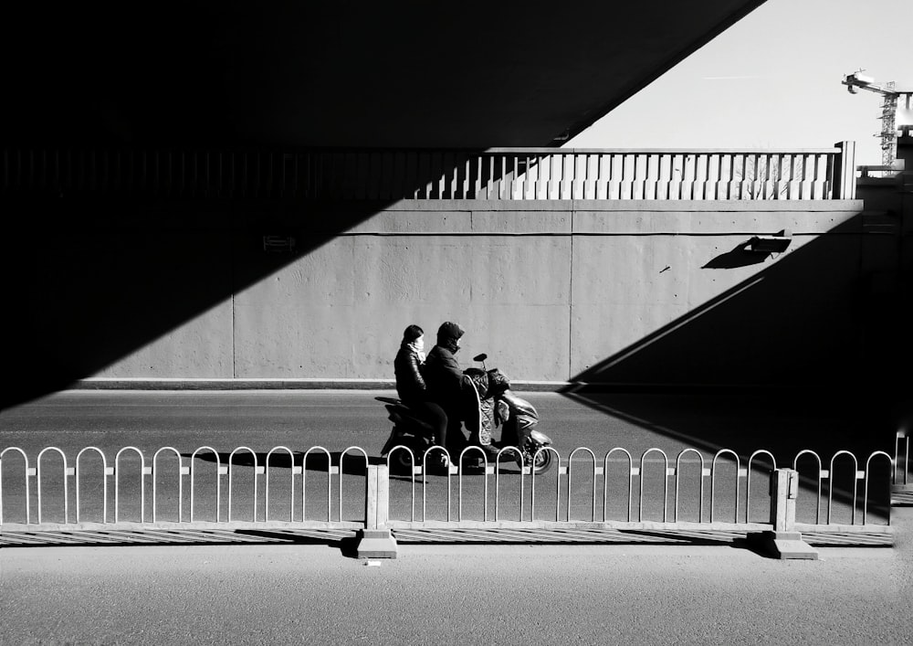 grayscale photo of two person sitting near fence