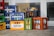 Several colored crates filled with various bottles are stacked and arranged outside. The bottles appear to contain drinks, with labels indicating different brands and types. The crates are in shades of blue, orange, green, and more, with some logos and text visible on them.