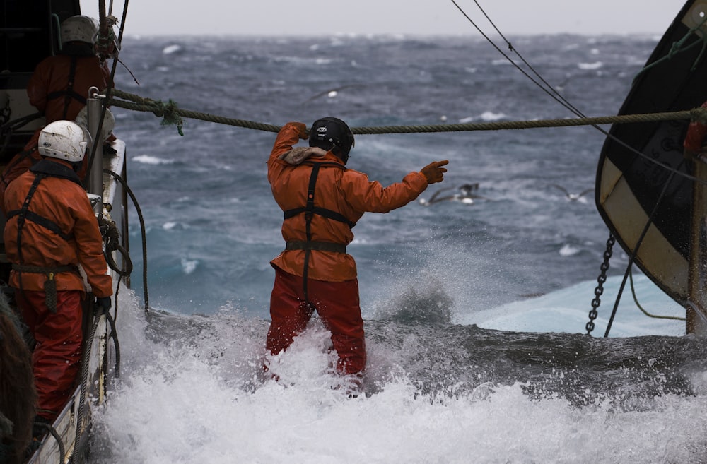 two man in orange coat crossing sea waves on focus photography