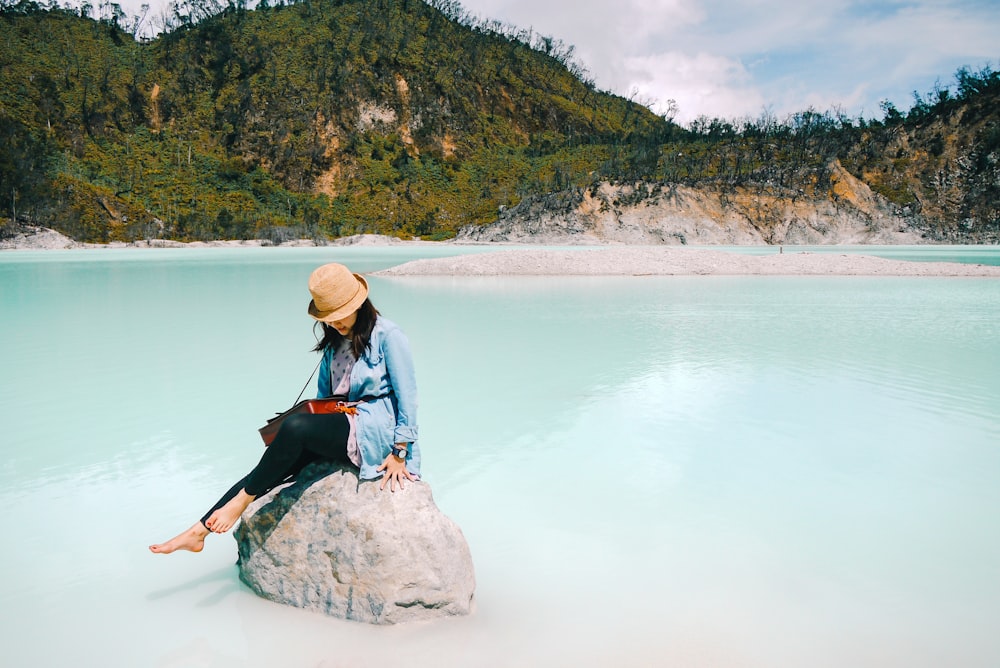 woman sitting on rock near body of water