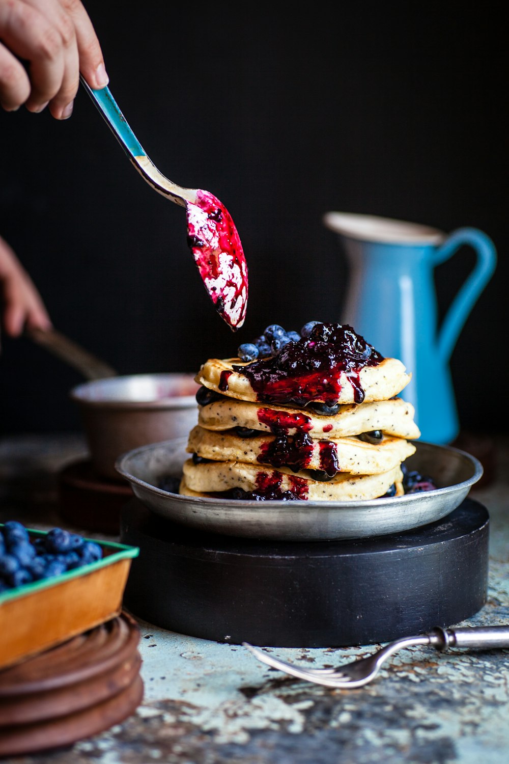 person holds spoons with berries near waffles on plate