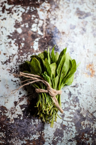 A bunch of tender baby spinach leaves glistening under soft light on a rustic wooden surface.