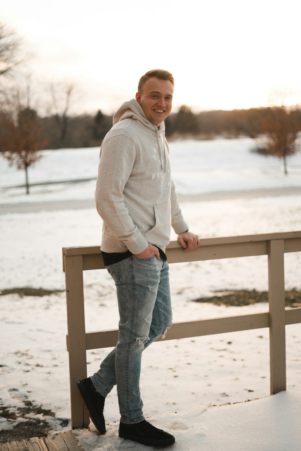 man wearing hoodie and blue jeans leaning on rail