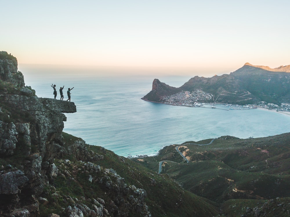 three people standing on ledge of mountain during daytime