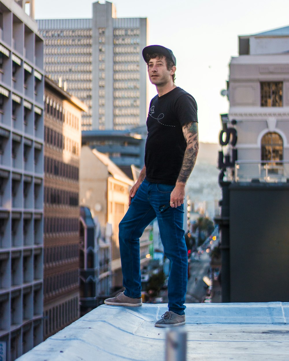 man wearing black tee shirt and blue pants standing on top of building