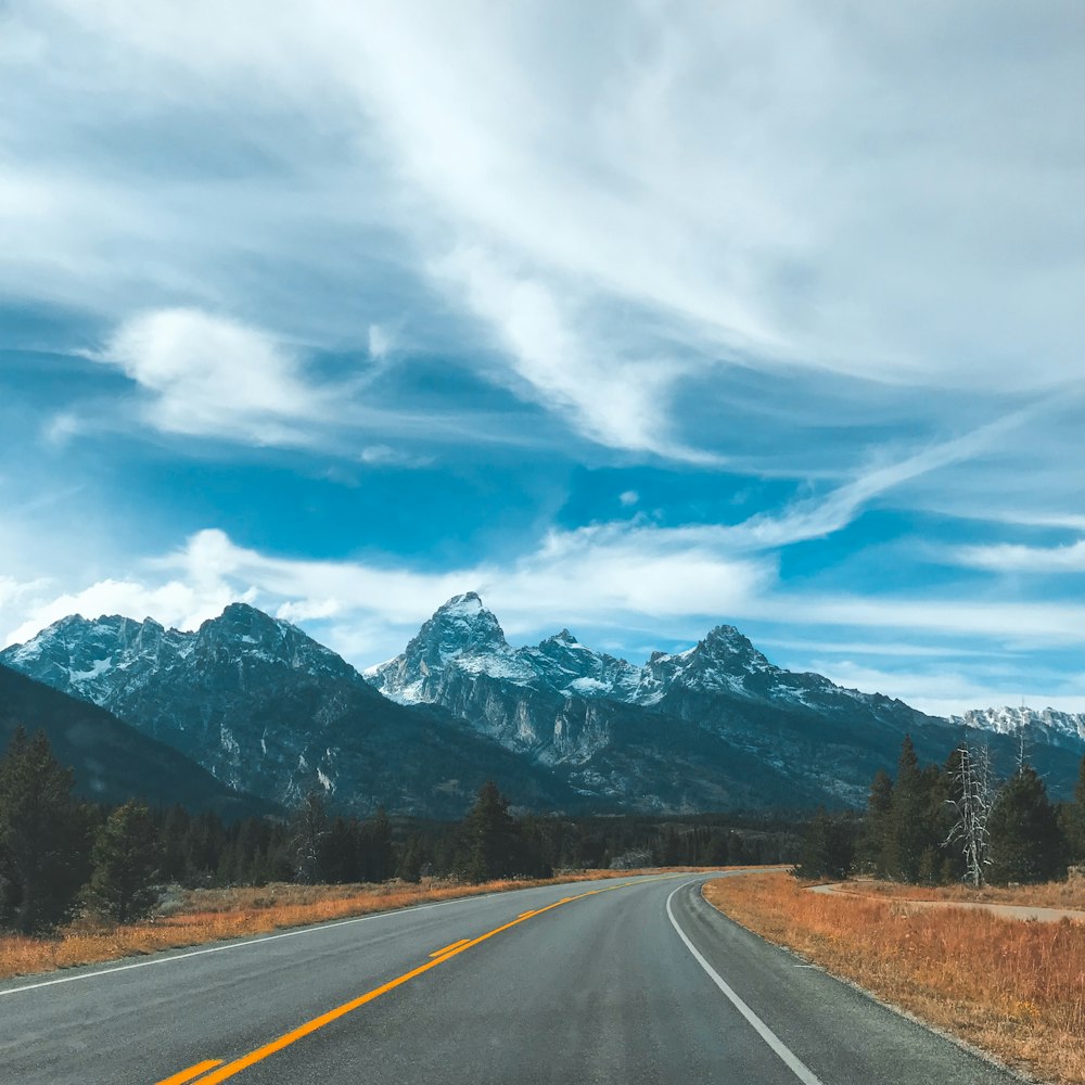 wide road near mountains under cloudy sky