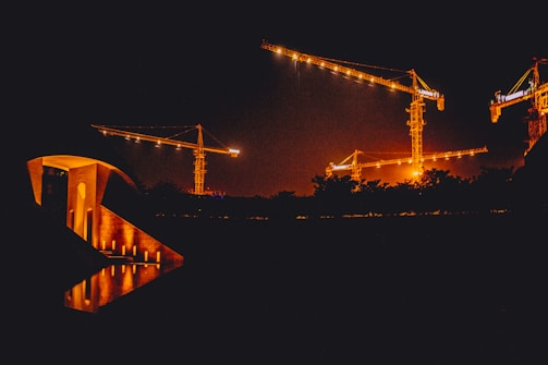 A sleek construction site at dusk showcasing cranes and steel frameworks illuminated by soft golden lights.