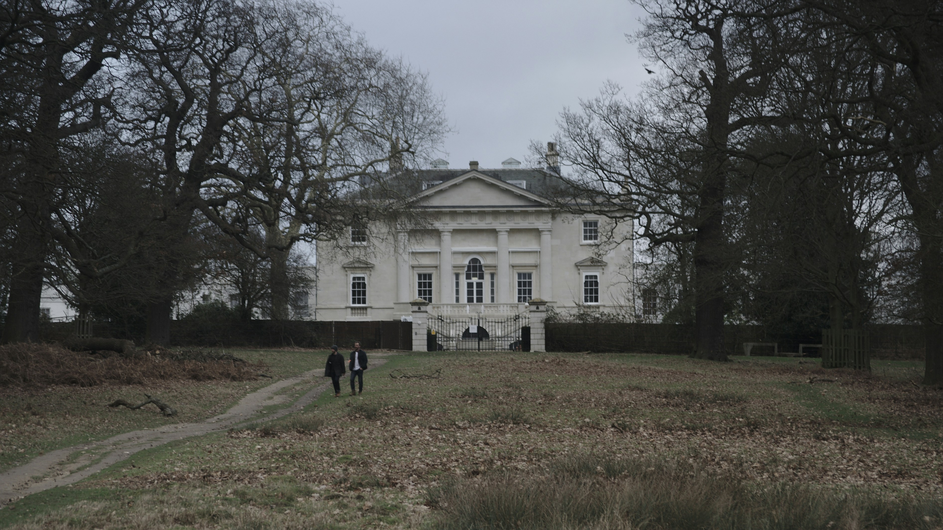 two person walking near house surrounded with trees