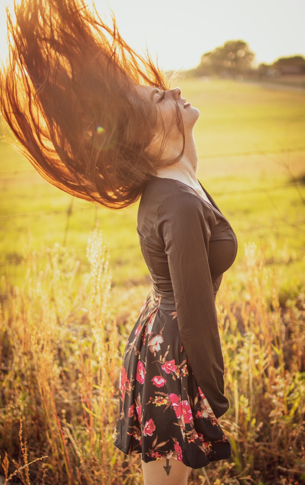 woman in black long-sleeved top and black and red floral mini skirt standing in grass field