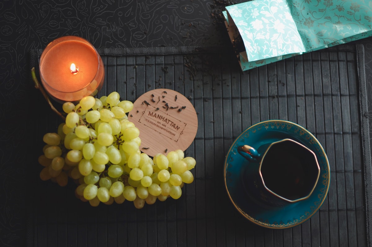 Racimo de uvas verdes sobre una mesa junto a una taza de cerámica