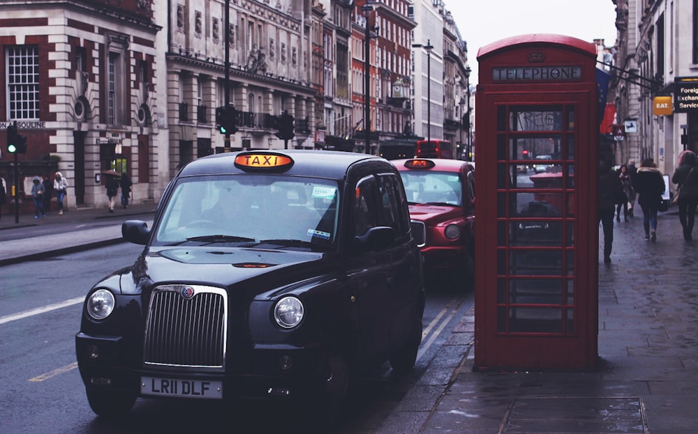 black Taxi beside telephone booth near people walking