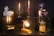 A variety of vintage projectors and mechanical objects are creatively transformed into lamps. The setup features six unique lamps, each with its own style and base, including film reels and gears. The lamps emit a warm, ambient light, casting a cozy glow.