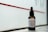 A bottle of beard oil with a dropper cap is placed on a ledge. The label reads 'Josè Manuel Hair Care Beard Oil' and notes the inclusion of mandarin, macadamia, and Abyssinian oil. The background consists of a red stripe on a frosted or translucent surface, allowing a subtle, diffused light to illuminate the bottle.