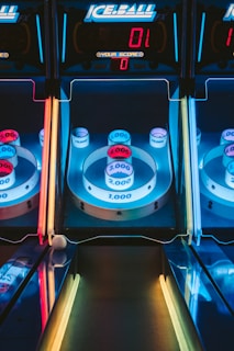 A skee-ball arcade game with illuminated targets displaying various point values, including 1,000, 2,000, 3,000, and 4,000. The colors are vibrant, with blue, red, and yellow neon lights surrounding the game. The digital scoreboard at the top reads a score of zero.
