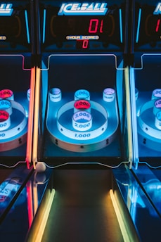 A skee-ball arcade game with illuminated targets displaying various point values, including 1,000, 2,000, 3,000, and 4,000. The colors are vibrant, with blue, red, and yellow neon lights surrounding the game. The digital scoreboard at the top reads a score of zero.