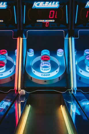 A skee-ball arcade game with illuminated targets displaying various point values, including 1,000, 2,000, 3,000, and 4,000. The colors are vibrant, with blue, red, and yellow neon lights surrounding the game. The digital scoreboard at the top reads a score of zero.