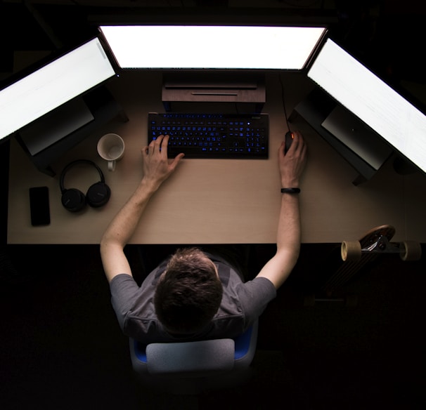 man facing three computer monitors while sitting