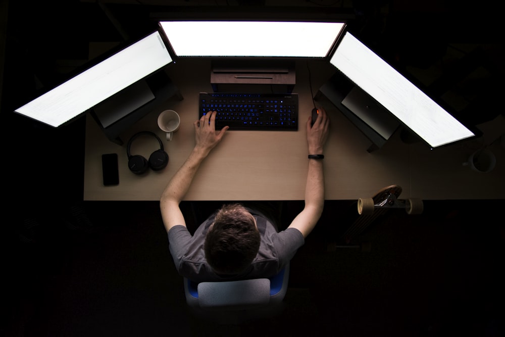 Hombre frente a tres monitores de computadora mientras está sentado