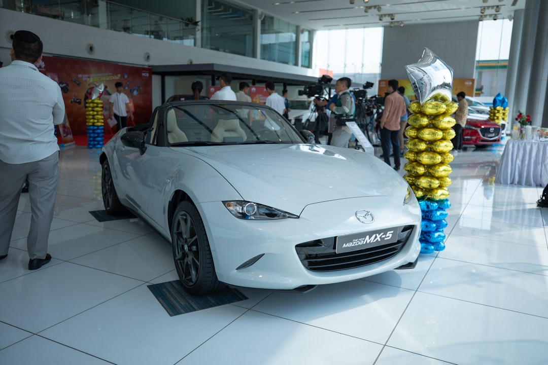 people near white Mazda MX-5 convertible coupe parked inside building