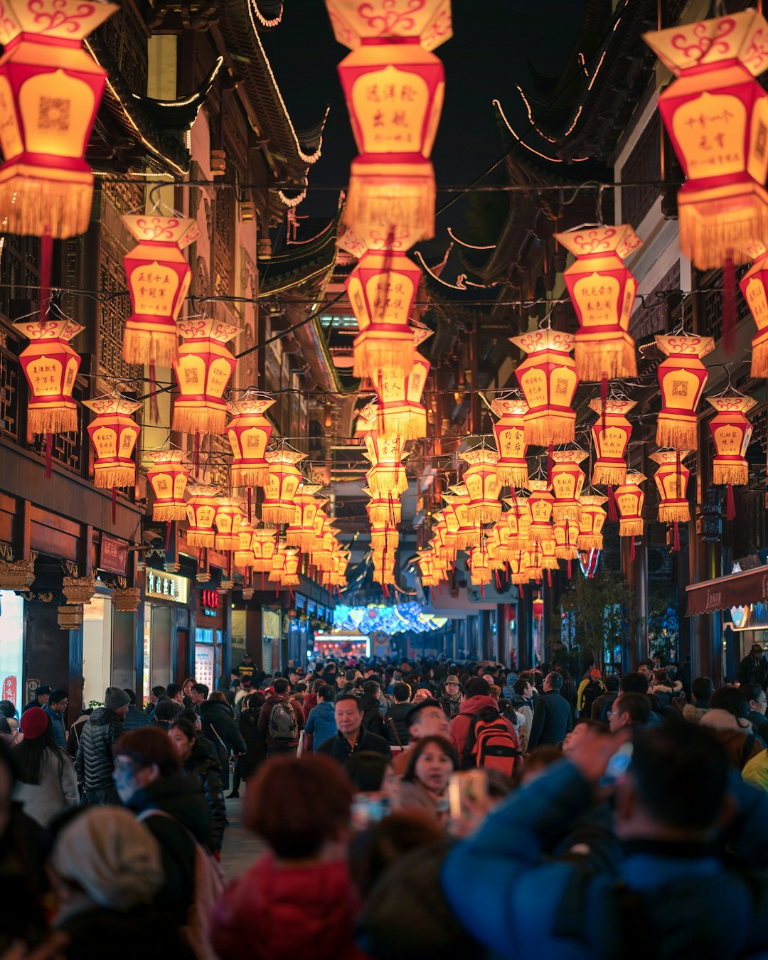 people walking between establishments with lanterns above