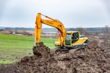 A large yellow excavator digging earth at a mining site under a clear blue sky.
